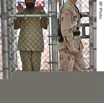 In this June 26, 2006 file photo, reviewed by US military officials, a detainee holds onto a fence as a US military guard walks past at the Guantanamo Bay US Naval Base, Cuba