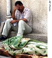 Sunni-Arab Shaabiya satellite television station employee sits next to body of his colleague at al-Kindi hospital, in Baghdad, October 12, 2006