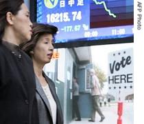 Pedestrians pass in front of share prices board with video screen in Tokyo, showing news on US elections