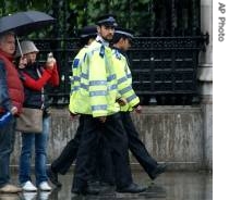 British police officers walk past tourists in the pouring rain in central London, 30 Jun 2007