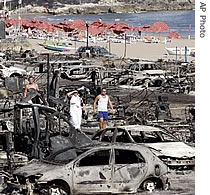 Vacationers walk past burnt cars at the San Nicola camping a day after a fire broke out, in Peschici, in the Gargano peninsula of the region of Puglia in Italy, 25 July 2007