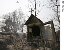 A burnt-out roadside shrine stands under a charred hillside as a water-dropping plane flies overhead near Ancient Olympia in southwestern Greece, 28 Aug. 2007