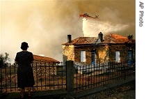 Woman watches her house as firefighting helicopter drops water in village of Thisoa, 29 Aug 2007