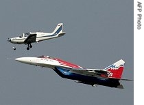 A MiG-35 aircraft flies under a propeller plane while taking part in the International Aviation and Space Salon 
