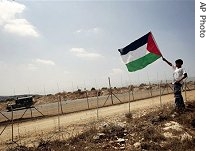 Palestinian boy holds a flag in West Bank village of Bilin as an Israeli army vehicle passes by a section of separation barrier during celebrations of Israeli Supreme Court's resolution to redraw route of the barrier, 04 Sept 2007